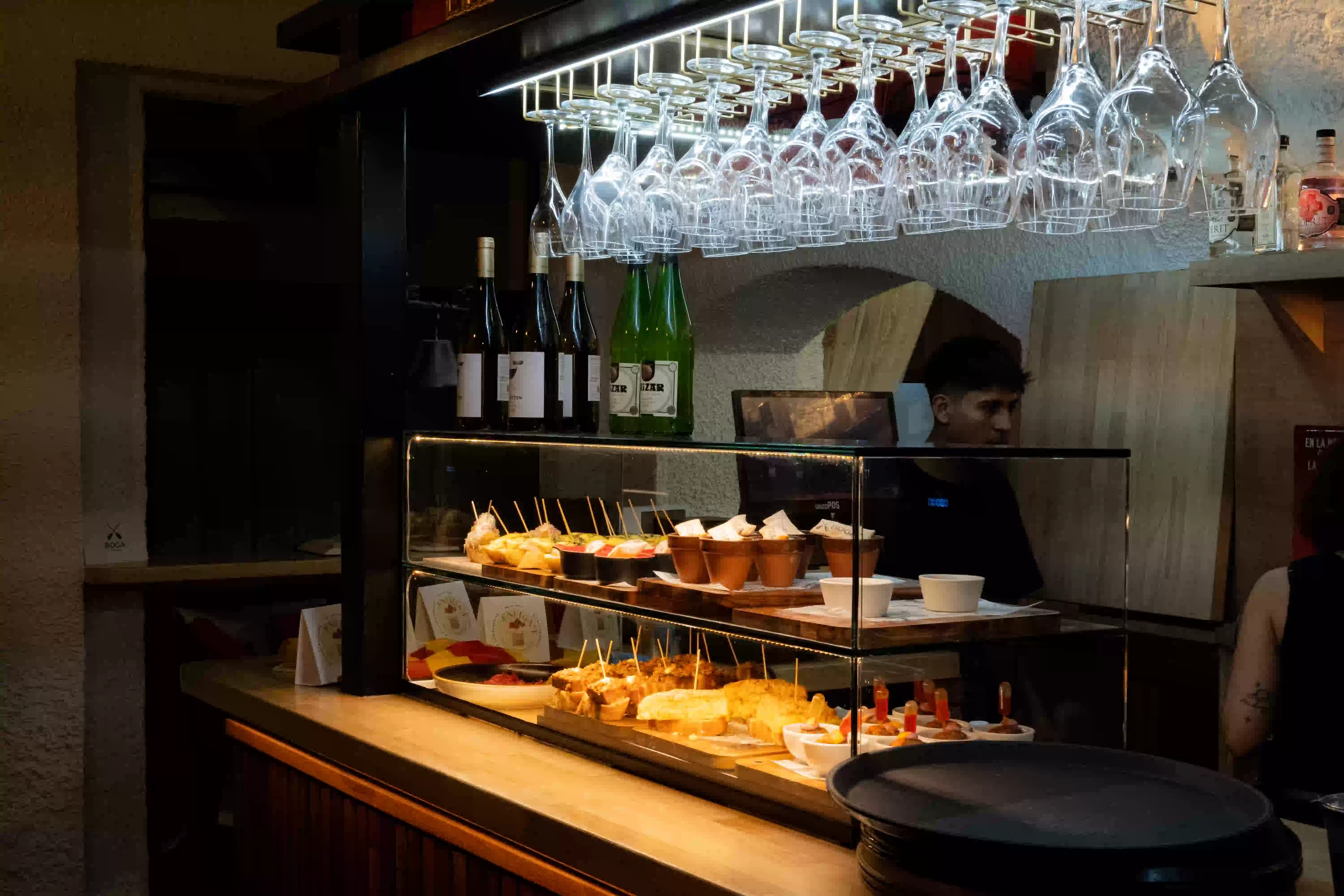 Barra de Boga con la vitrina de pintxos, las copas colgadas del techo y un camarero al fondo