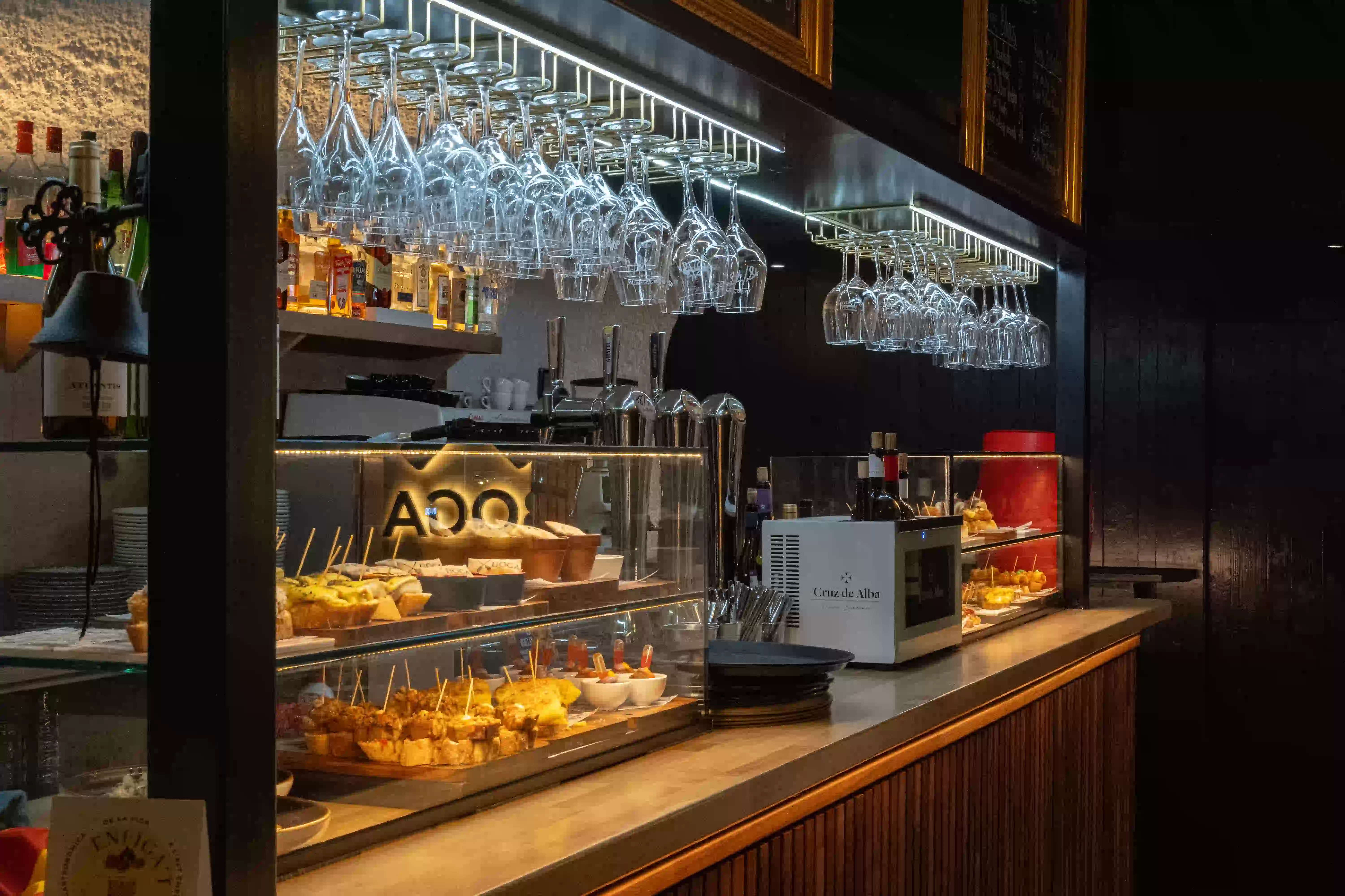 Barra de Boga en penumbra con la vitrina de pintxos, los tiradores de cerveza y las copas colgadas