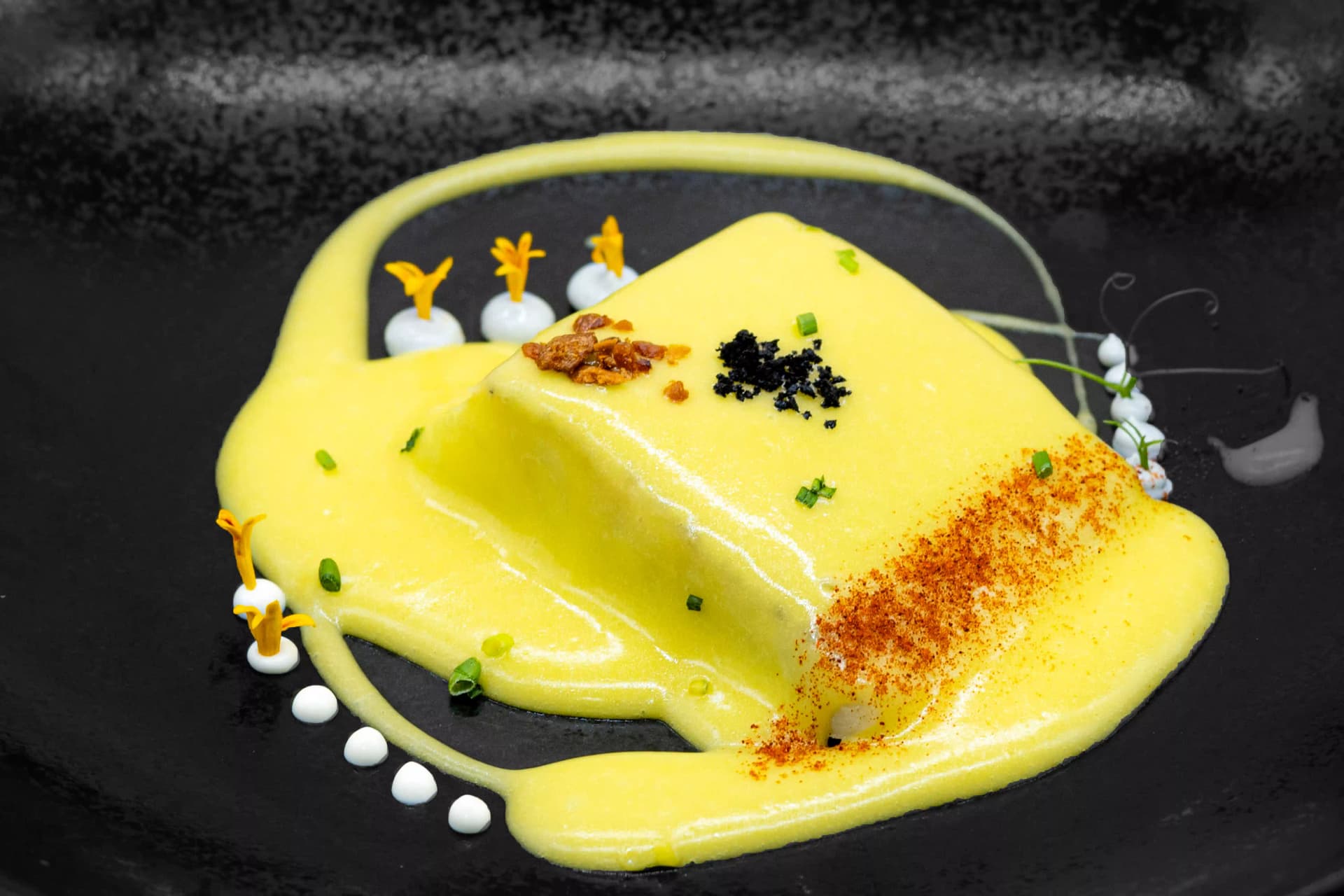 Lomo de bacalao napado en salsa amarilla sobre plato negro, con pimentón, huevas y puntos de crema
