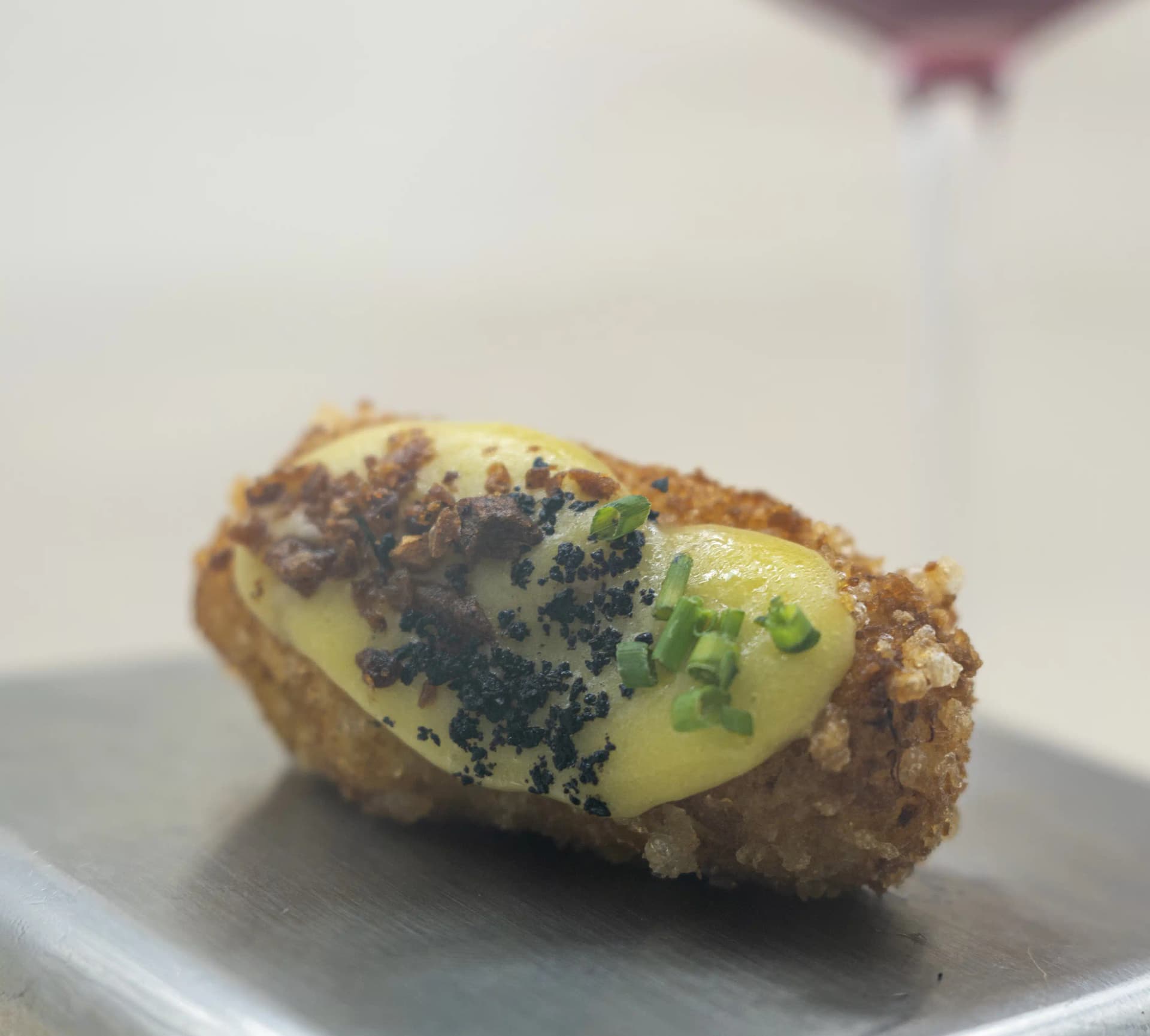 Croqueta casera recién frita con una quenelle de crema, huevas negras y cebollino, sobre bandeja metálica